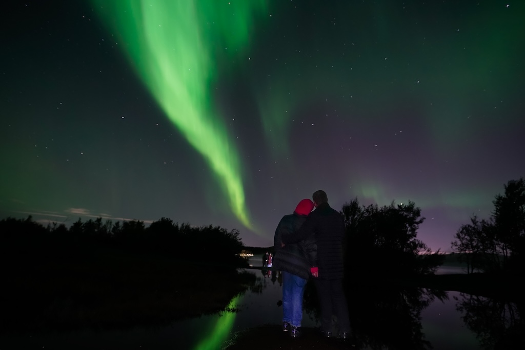 A couple watching green northern lights reflected in a lake