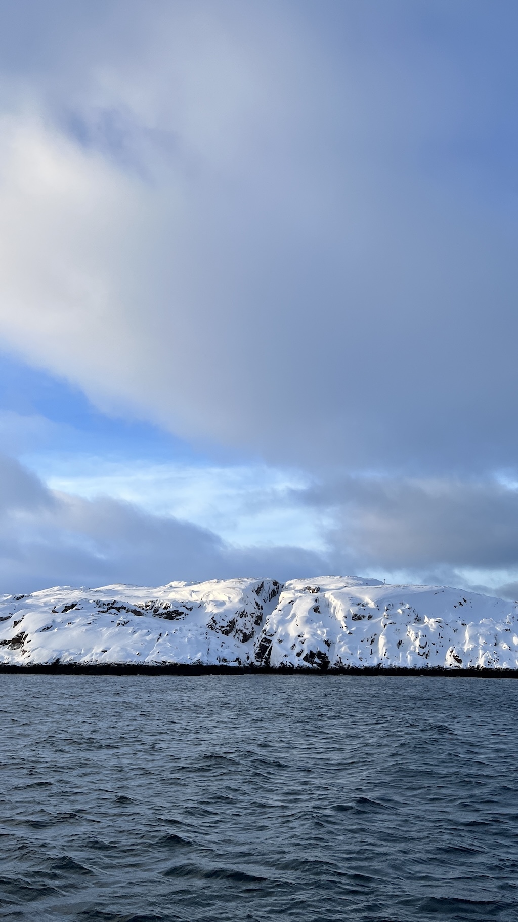 Snow-covered coastal cliffs seen across the sea