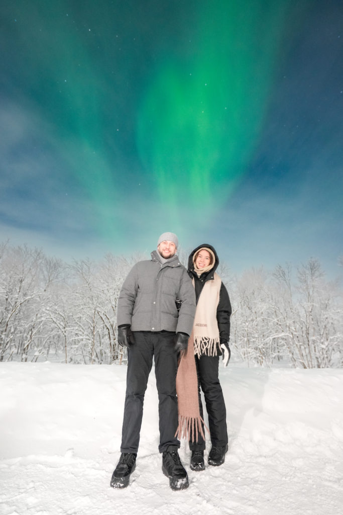 Guests beneath the aurora beside snowy trees